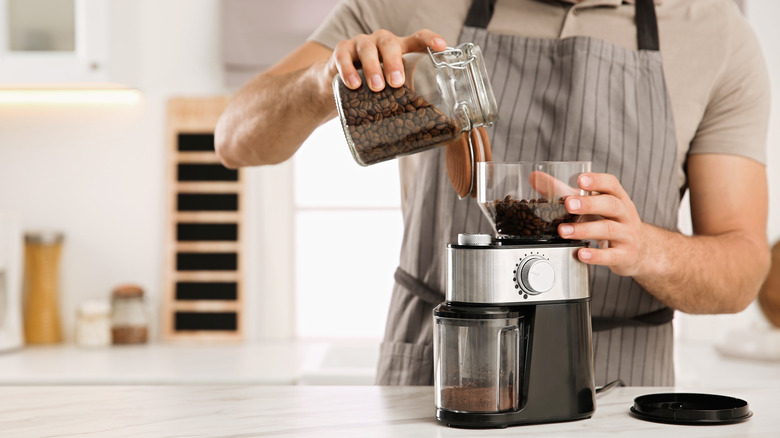 man pouring coffee beans into burr grinder