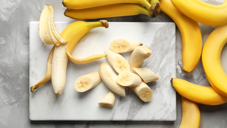 Sliced bananas on top of cutting board with whole bananas sitting on the right