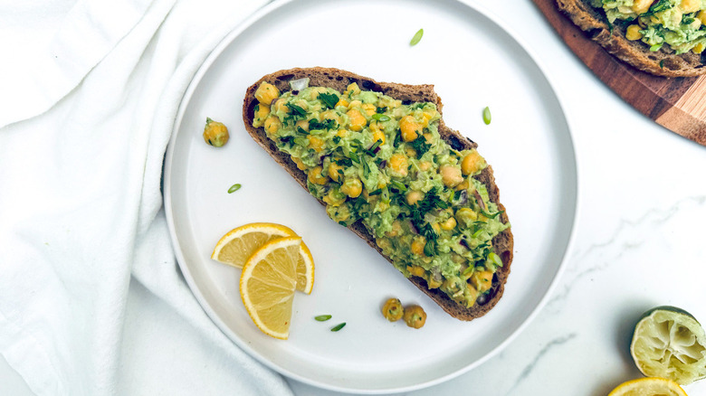 chickpea avocado toast on white plate with lemon slice